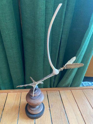 Sculpture d'une pâte d'oiseau prolongée de 2 ailes en laiton doré et surmontée d'une côte monté sur socle circulaire en bois.