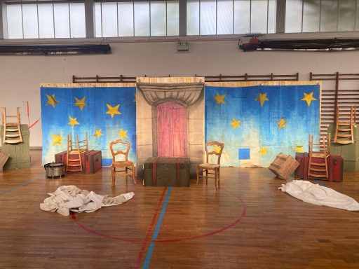 Décor de scène avec 3 paneaux peints montrant une nuit étoilée devant une porte Haussmannienne et  accessoires devant (Chaises, coffres).